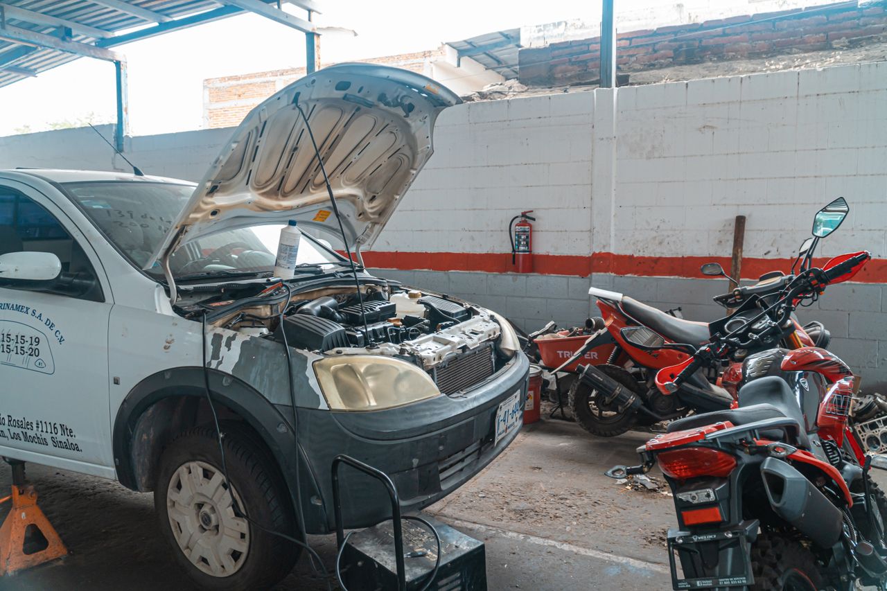 Car being repaired in a garage with motorcycles and tools around.